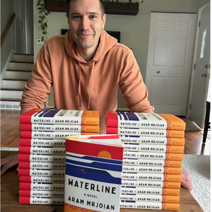 Aram Mrjoian, Northwestern MFA alum, stands with stacks of his new book Waterline at a table.
