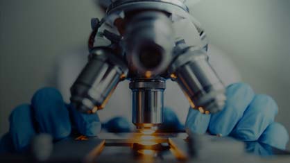 close up of lab technician wearing rubber gloves using microscope