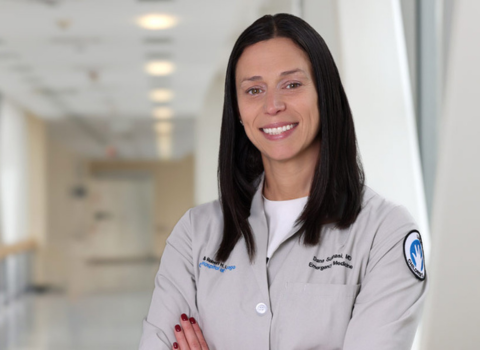 Dana Schinasi graduated with a Northwestern master's in Health Informatics. She wears a md jacket and has her arms crossed, standing in a modern glass interior bridge