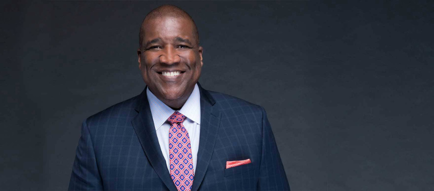Curt Menefee wears suit and big smile for a headshot. He is the keynotes speaker for SPS Convocation 2025.