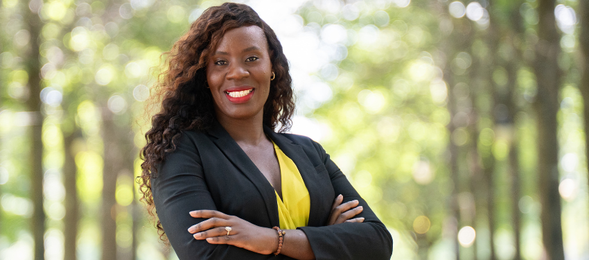Rose Kargbo in a park at Iowa, with green trees lining the street on a beautiful sunny summer day. She wears a professional suit, bright yellow top, and has her arms crossed in a professional pose. Rose graduated with an MS in Global Health from Northwestern SPS in 2023.