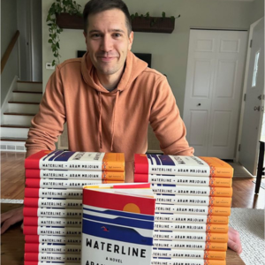 Aram Mrjoian, Northwestern MFA alum, stands with stacks of his new book Waterline at a table.